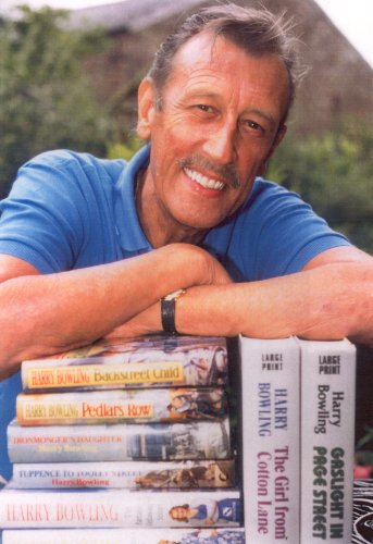 Man smiling, leaning on a stack of books by Harry Bowling.