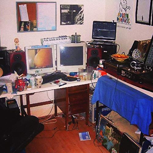 A cluttered music production desk with two computer monitors, speakers, and various electronic equipment.