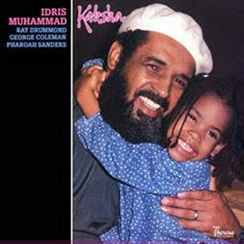 Idris Muhammad wearing a white cap and smiling while hugging a young girl.