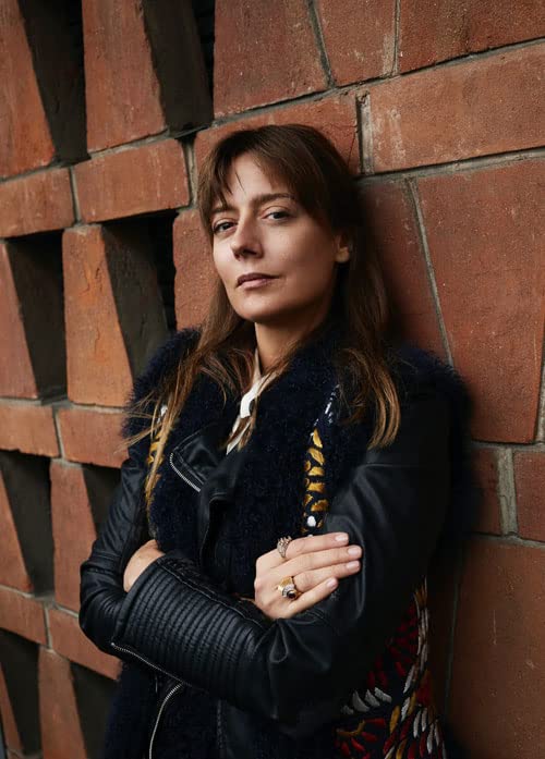 Woman in a black leather jacket leaning against a brick wall.