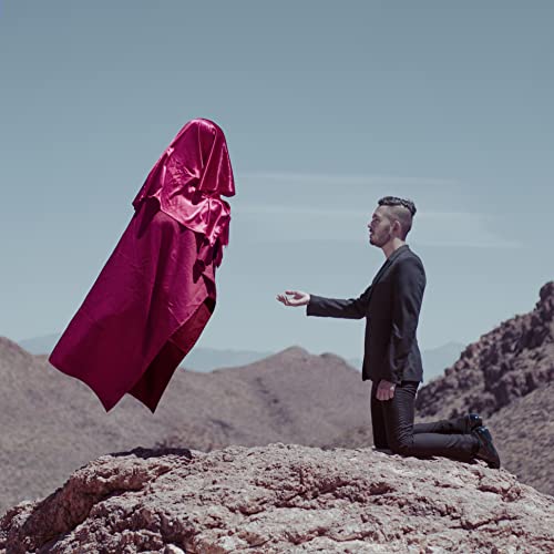 Man kneels before a floating, draped figure in a desert landscape.