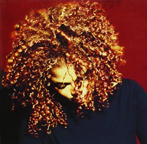 Janet Jackson with long curly hair looking down against a dark red background.