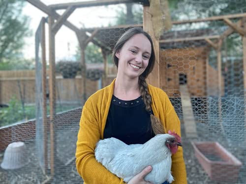 Woman holding a white chicken in front of a chicken coop.