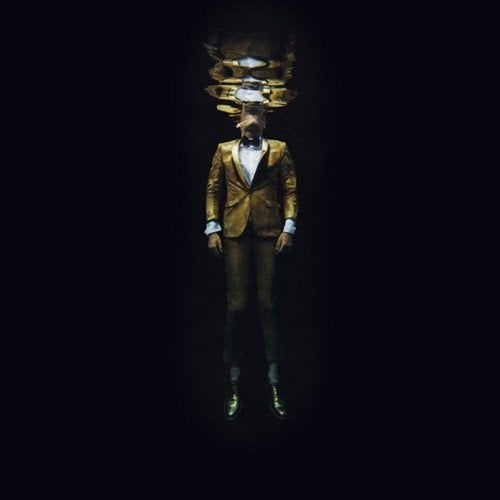 Man in gold suit stands against black background, headless with reflections above.