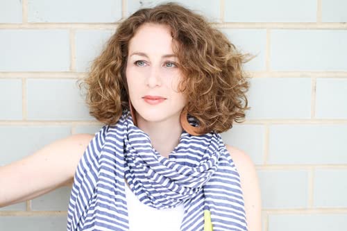 Woman with curly hair wearing a striped scarf against a brick wall.