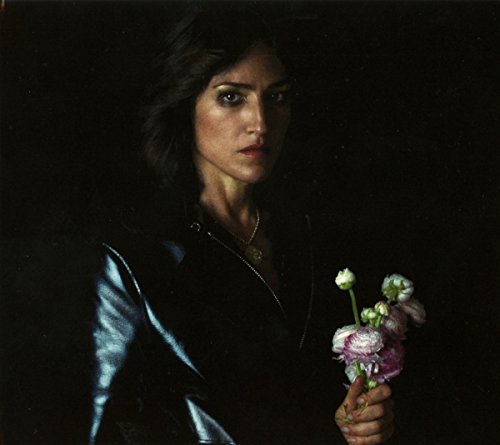 Woman with dark hair and a black jacket holding pink flowers against dark background.