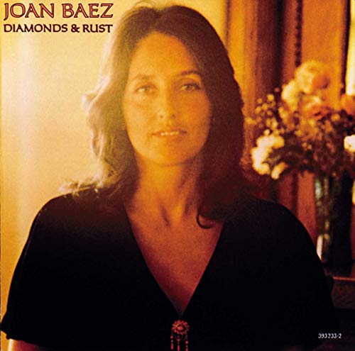 Portrait of Joan Baez in a black dress with a vase of flowers behind her.