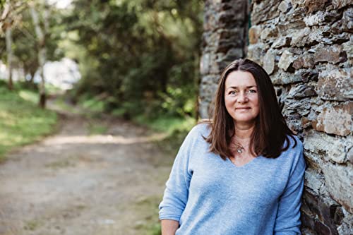 Woman with brown hair leans against a stone wall outdoors.