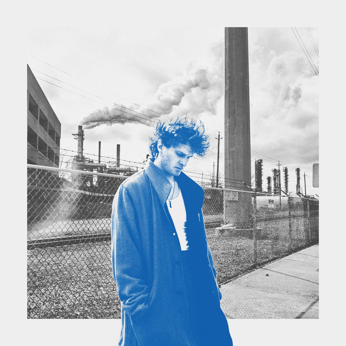 Man in blue coat stands before an industrial landscape.