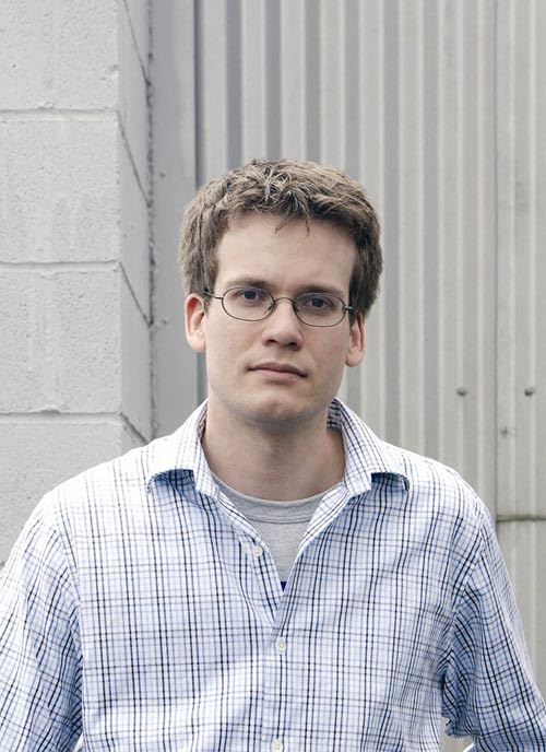 Young man with short brown hair and glasses, wearing a plaid shirt.