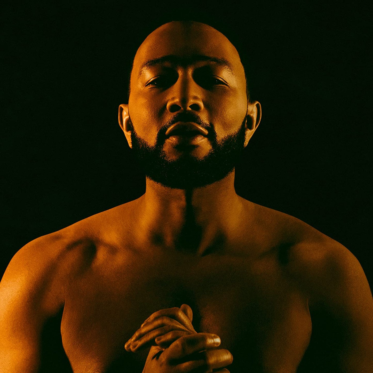 "John Legend's album cover featuring a shirtless man with hands clasped, lit with orange glow."