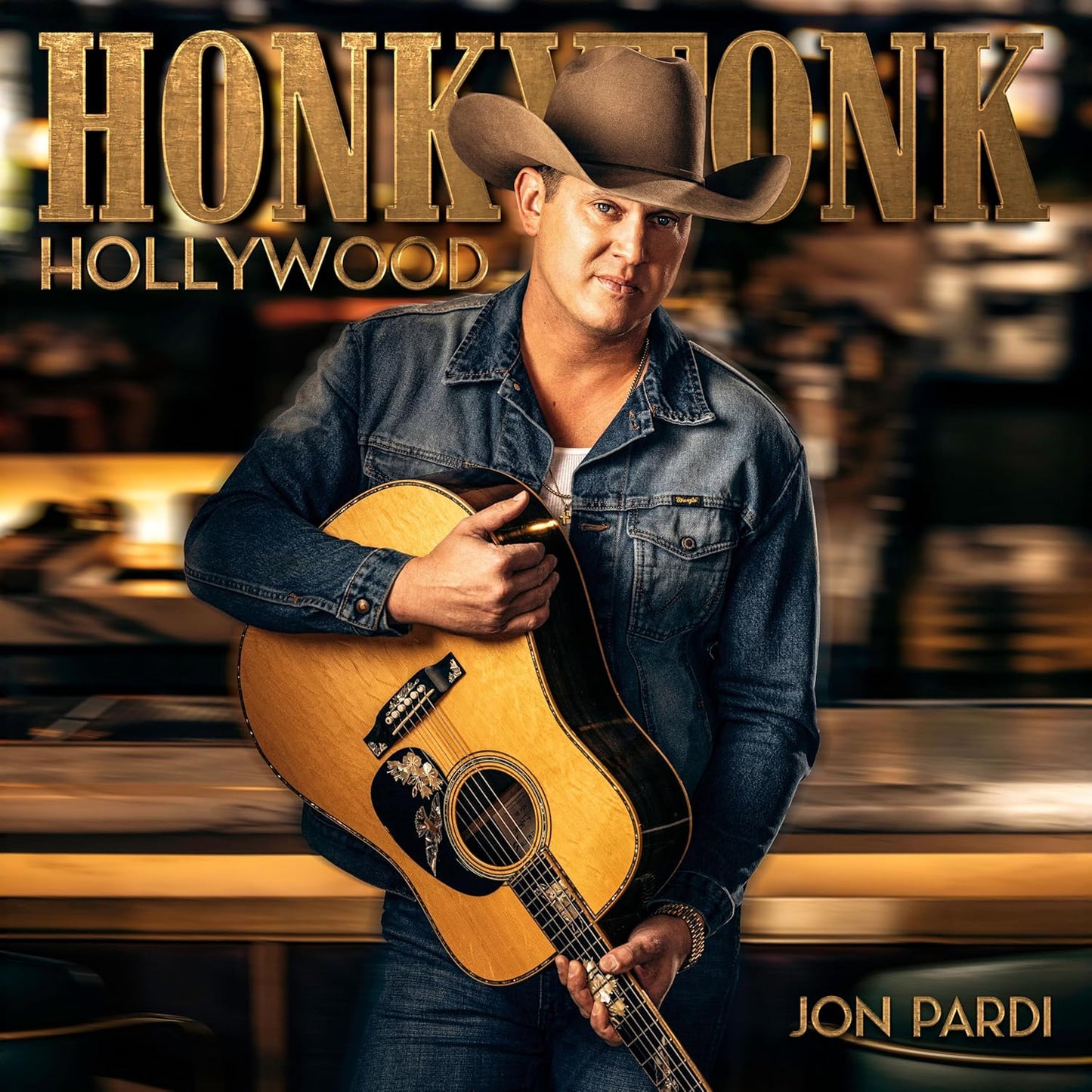 Jon Pardi wearing a cowboy hat and denim jacket holding an acoustic guitar.