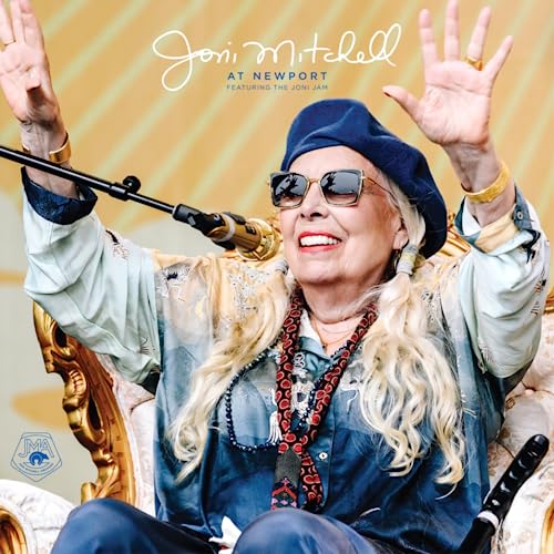 Joni Mitchell smiling with a microphone, wearing a beret and sunglasses.