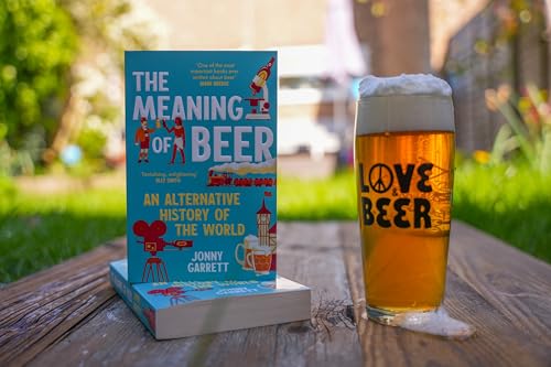 The book The Meaning of Beer next to a glass of beer outdoors.
