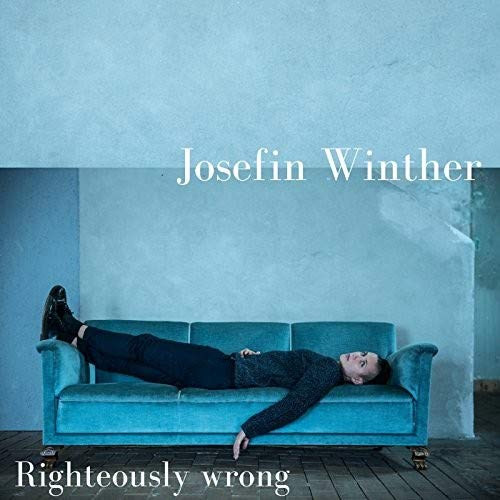 "Album cover with a woman lying on a blue couch against a blue wall."
