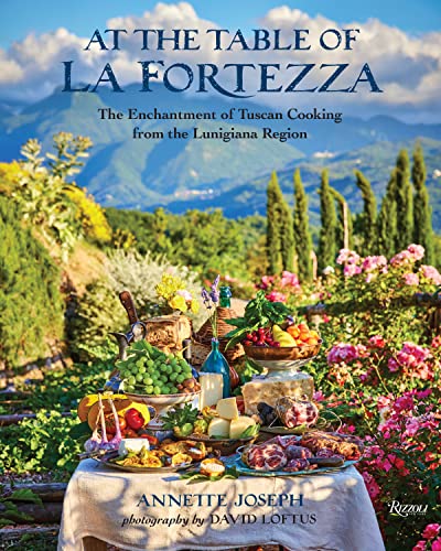 Cookbook cover with a table laden with food and a Tuscan landscape.