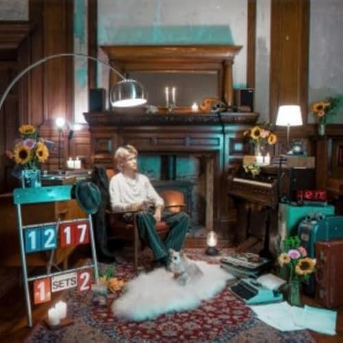 A person sits in a chair in a vintage room with a dog nearby.
