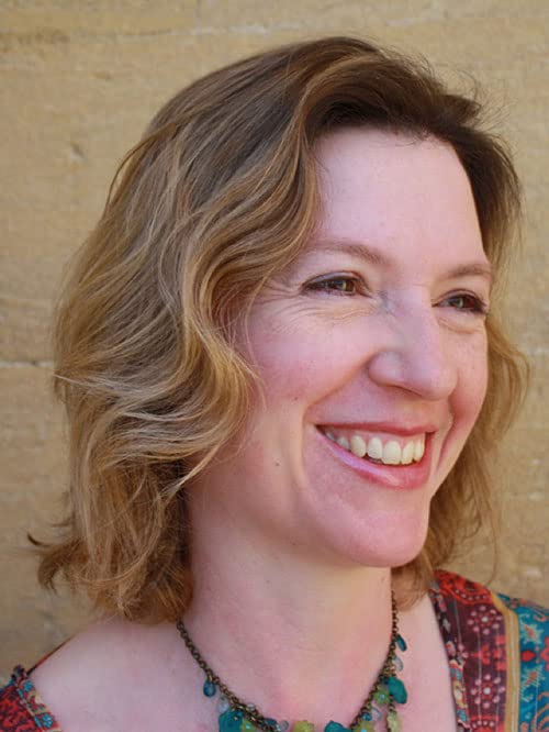 Close-up portrait of a smiling woman with wavy blonde hair and a colorful necklace.