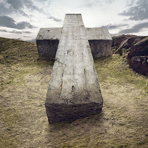 Concrete cross stands in a grassy, rocky landscape under a cloudy sky.