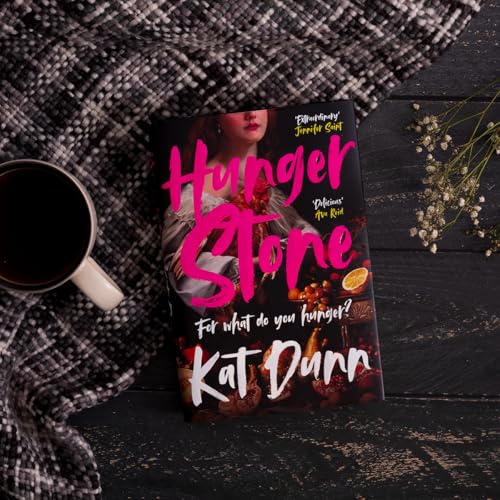 Book cover for Hungerstone by Kat Dunn next to a coffee mug and flowers.