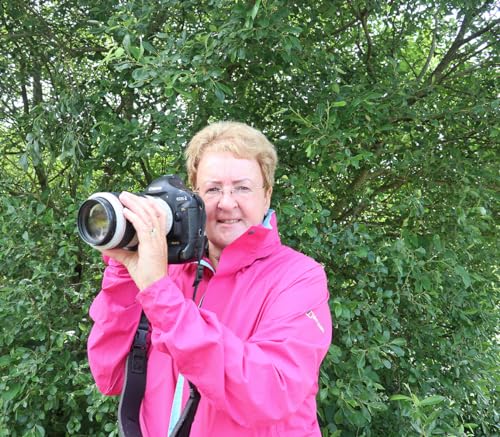 Woman with short hair holding a DSLR camera outdoors.