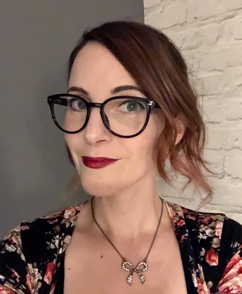 Woman with red-brown hair and glasses, wearing a floral top.