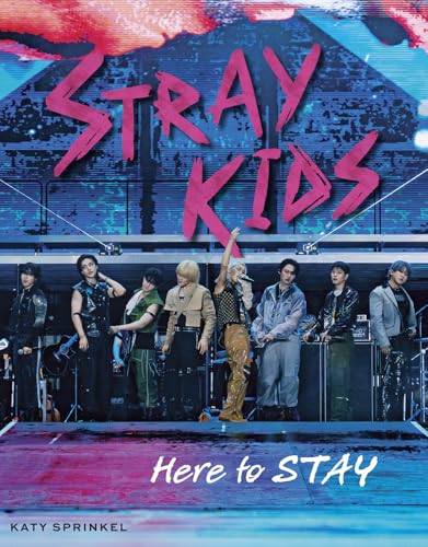 The Stray Kids boy band stands on a concert stage under large pink text.