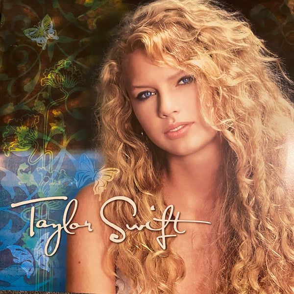 Close-up portrait of Taylor Swift with long, wavy blonde hair and floral design.