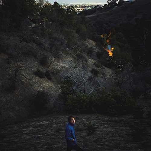 Man walking on hillside with burning bushes in the background.