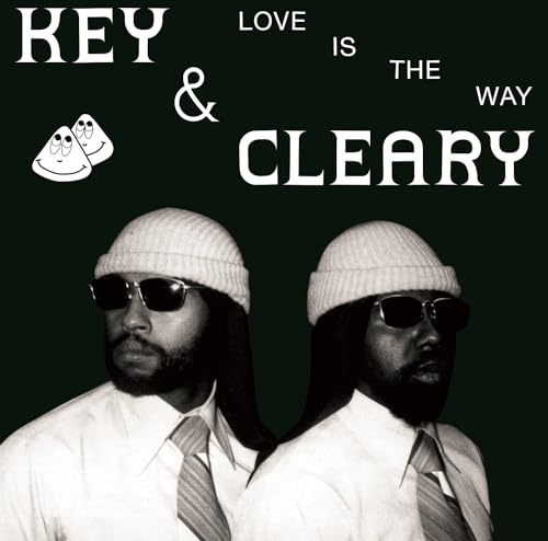 Two men wearing white beanies, sunglasses, and ties against a black background.