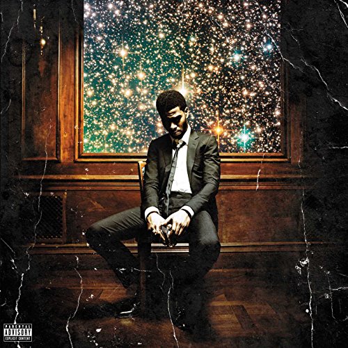 Kid Cudi in a suit sits before a window displaying a starry night.