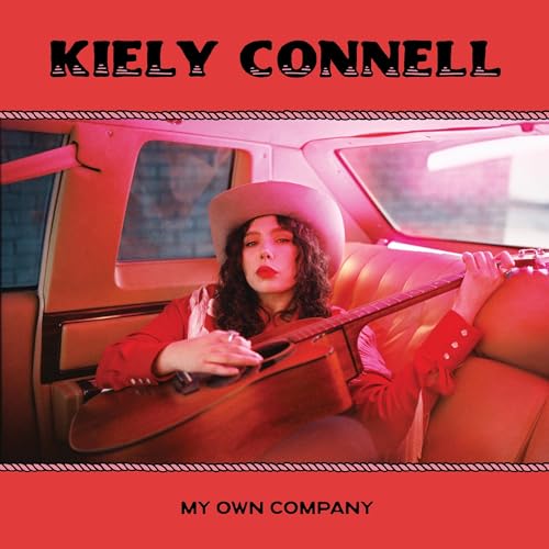 Kiely Connell with guitar inside a vintage car, album cover.