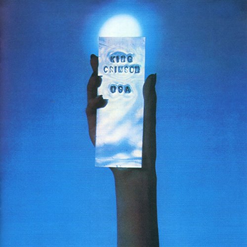 A hand holds a rectangular silver object against a bright blue background.