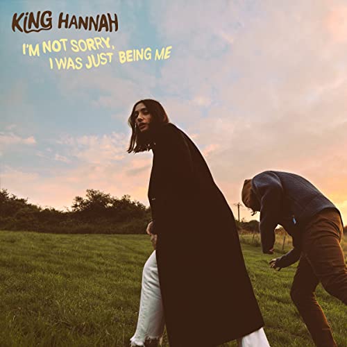 CD cover: woman in black coat walking in a grassy field.