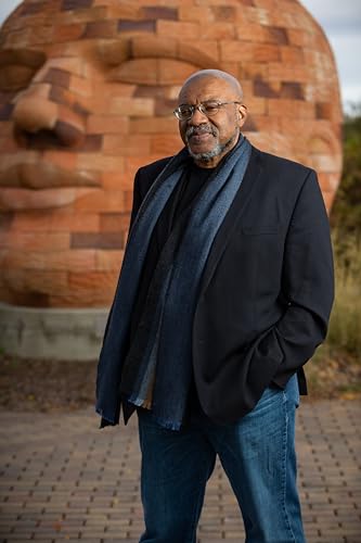Portrait of a man with a large brick head sculpture behind him.