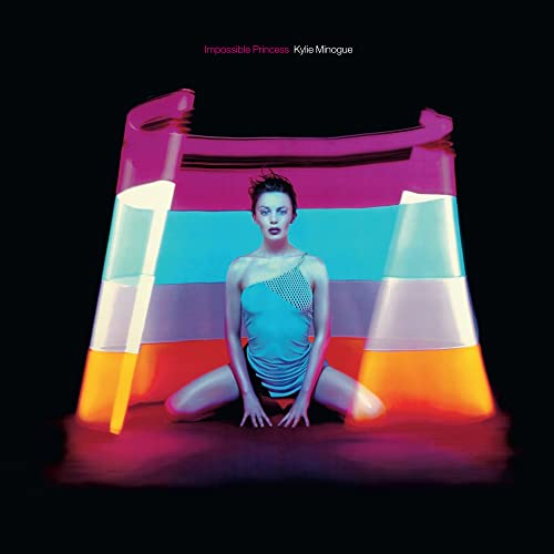 Kylie Minogue sits before a colorful, inflatable archway on a black background.