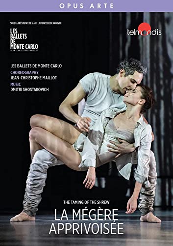 A male and female ballet dancer performing a lift on a dark stage.