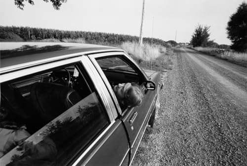 Black and white photo of a person looking out of a car window.