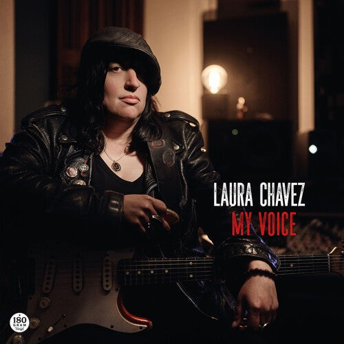 Laura Chavez poses with a guitar, wearing a leather jacket and cap.
