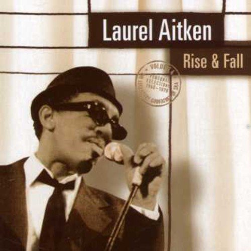 Laurel Aitken in a hat and sunglasses, singing into a microphone.
