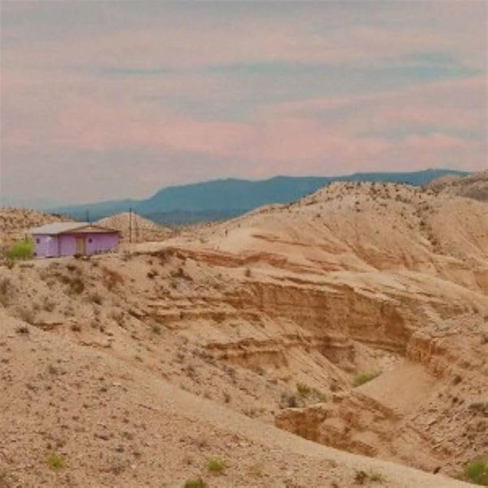 Desert landscape with a small, pale purple building under a pink sky.