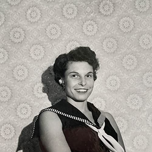 Black and white portrait of a smiling woman wearing a sailor-style collar against wallpaper.