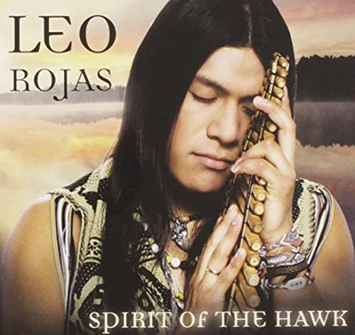 Leo Rojas holding a pan flute against a sunset background with lake and trees.
