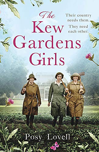 Three women in work clothes walk through a garden with a greenhouse in background.