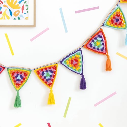 A colorful crochet bunting with triangular granny square flags and tassels hanging on a wall.