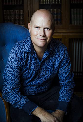 A bald man in a blue patterned shirt sitting in a blue chair.