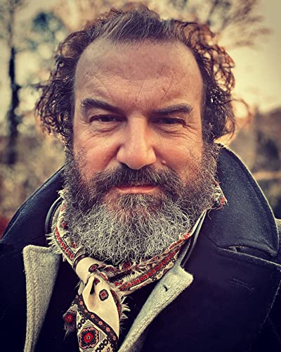 Close-up portrait of a bearded man wearing a patterned neckerchief and dark coat.