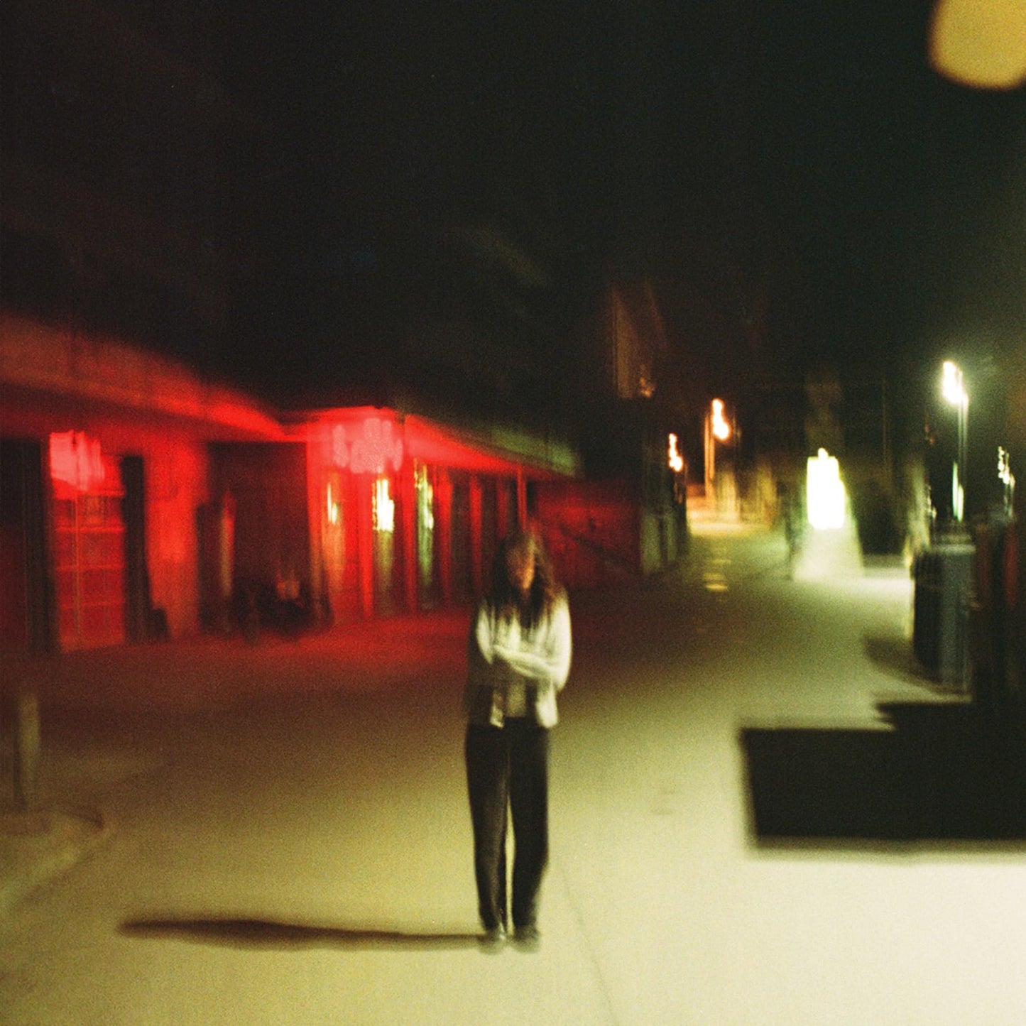 A person stands on a dark street at night with red and yellow lighting.