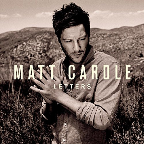 Sepia-toned portrait of Matt Cardle standing in a field with hands clasped together.