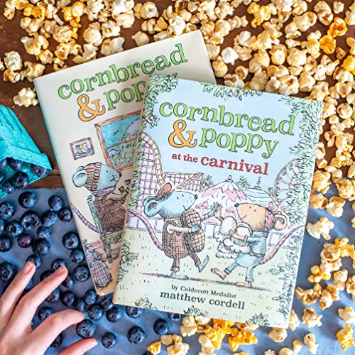 Children’s book “Cornbread & Poppy at the Carnival” surrounded by popcorn and blueberries.